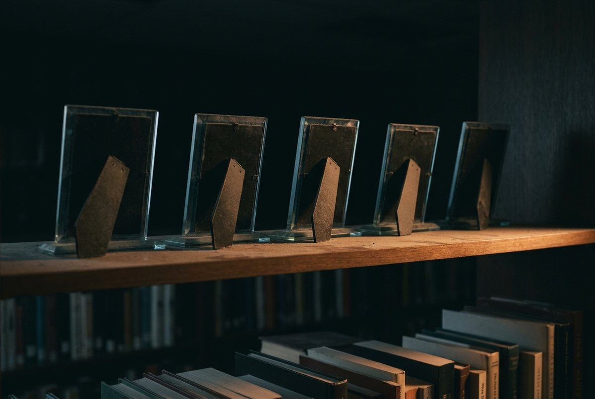 A row of awards on a wooden shelf, all turned to face the wall, above shelves of books.